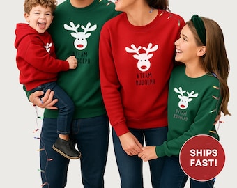 May include: A family wearing matching Christmas sweaters. The sweaters are red and green with a white reindeer design and the text "#TEAM RUDOLPH" or "#TEAM DOLPH". The family is smiling and appears to be happy.