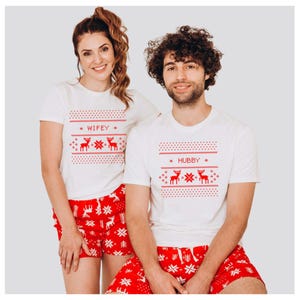 Puede incluir: Conjunto de camisetas blancas y pantalones cortos rojos a juego con temática navideña. Las camisetas llevan las palabras "Wifey" y "Hubby" con diseños de renos y copos de nieve. Los pantalones cortos son rojos con estampados de copos de nieve blancos.