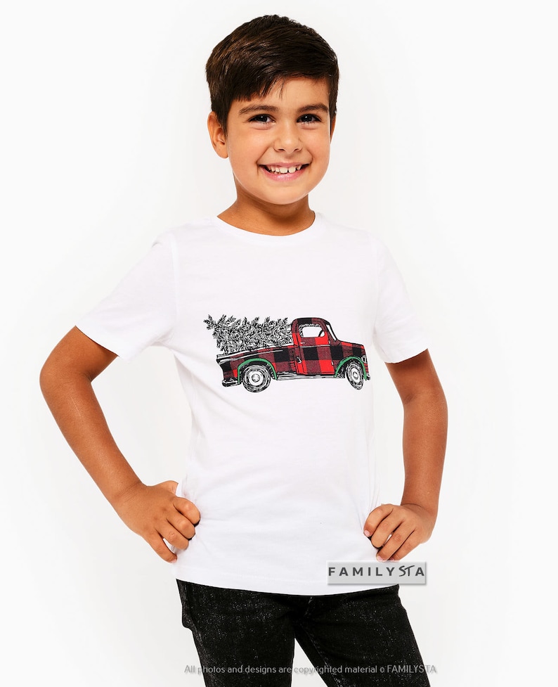 May include: White t-shirt with a red and black plaid pickup truck carrying a Christmas tree. The truck has a green steering wheel and green wheels. The text "FAMILYSTA" is on the bottom right corner of the shirt.