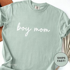 K&ouml;nnte beinhalten: Hellgr&uuml;nes T-Shirt mit dem wei&szlig;en Schriftzug "boy mom" in Schreibschrift. Das Shirt hat eine einfarbige Farbe und einen Rundhalsausschnitt. Die Farbe ist mit "Bay" bezeichnet.
