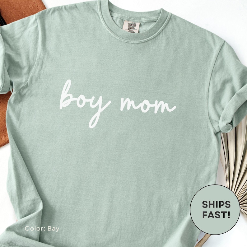 K&ouml;nnte beinhalten: Hellgr&uuml;nes T-Shirt mit dem wei&szlig;en Schriftzug "boy mom" in Schreibschrift. Das Shirt hat eine einfarbige Farbe und einen Rundhalsausschnitt. Die Farbe ist mit "Bay" bezeichnet.