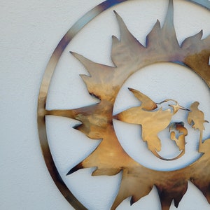 May include: A metal wall art piece in the shape of a sun with a hummingbird flying through it. The sun is a golden colour and the hummingbird is a lighter gold colour.