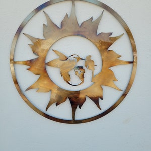 May include: A circular metal wall art piece with a sunburst design. The sunburst is made of metal and has a brown and gold finish. A hummingbird is silhouetted in the centre of the sunburst.