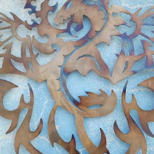 May include: A metal dragon sculpture with intricate details, cut out in a stylized design. The dragon is brown with a blue iridescent sheen, and is mounted on a blue wall.