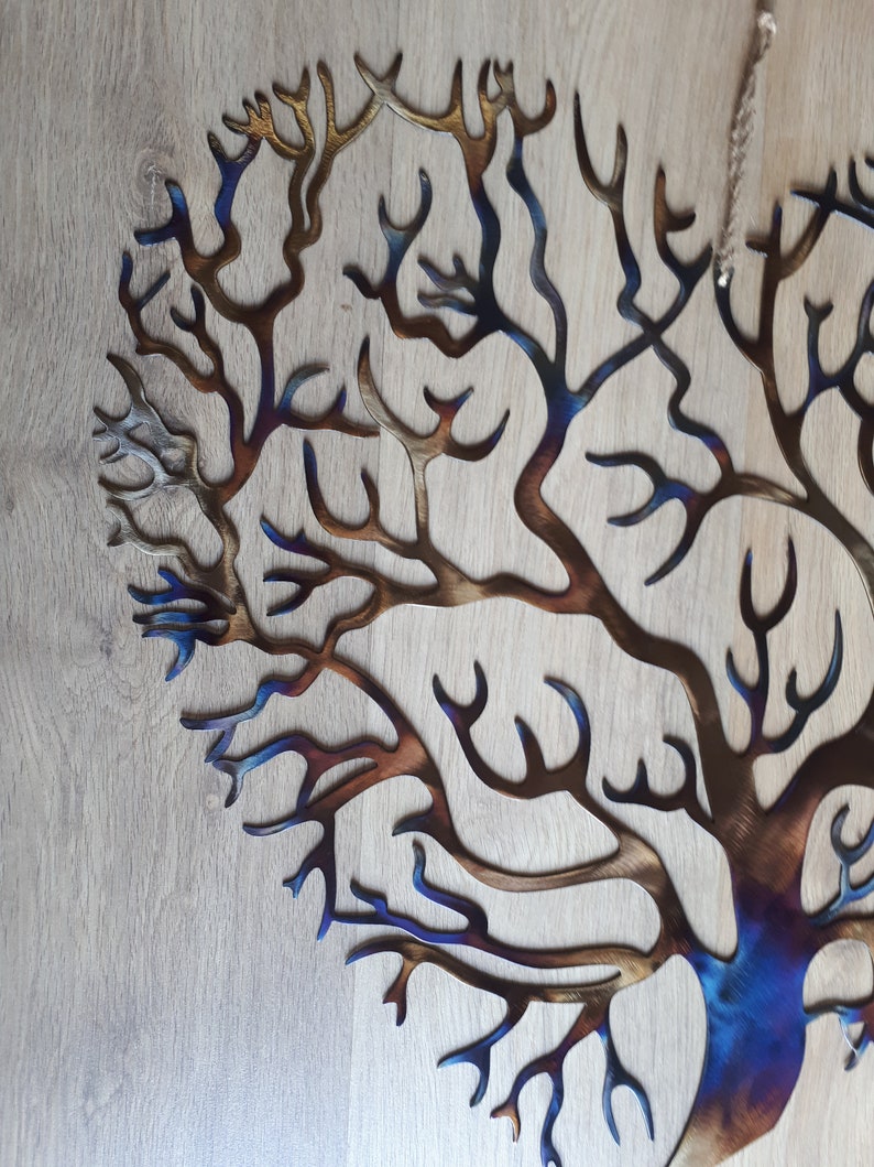 K&ouml;nnte beinhalten: Eine Wandskulptur aus Metall, die einen Baum mit einem Farbverlauf von Blau, Braun und Gold darstellt. Der Baum besteht aus d&uuml;nnem Metall und hat ein filigranes, kompliziertes Design.
