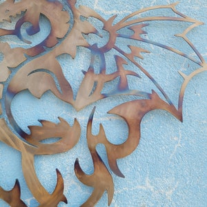 May include: A metal dragon wall art sculpture with a brown and blue patina. The dragon is in a curled position with its wings spread out.
