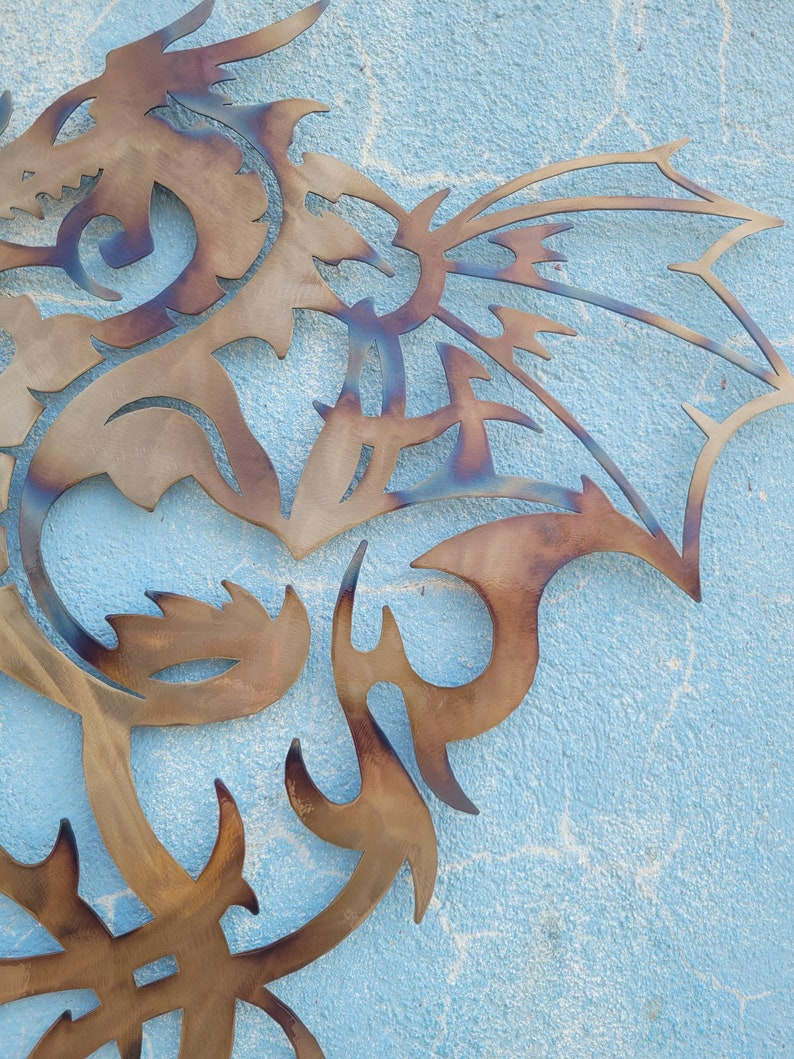 May include: A metal dragon wall art sculpture with a brown and blue patina. The dragon is in a curled position with its wings spread out.