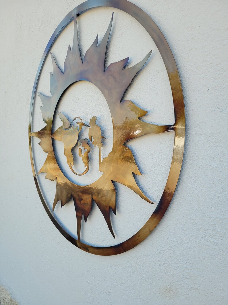 May include: A circular metal wall art piece with a sunburst design in gold and brown tones. The sunburst is centred in a circle with a silhouette of three birds inside.