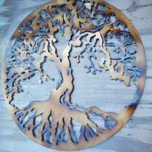 Op de afbeelding: Een metalen wandsculptuur van een boom met ingewikkelde takken en wortels. De sculptuur is rond en heeft een rustieke, gebrande afwerking in tinten bruin en blauw.