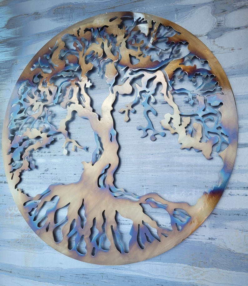 Op de afbeelding: Een metalen wandsculptuur van een boom met ingewikkelde takken en wortels. De sculptuur is rond en heeft een rustieke, gebrande afwerking in tinten bruin en blauw.