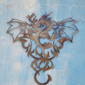 May include: A metal wall decor featuring a stylized dragon with intricate details. The dragon is depicted with wings spread wide and a long, flowing tail. The metal is a warm brown color, giving the piece a rustic look.