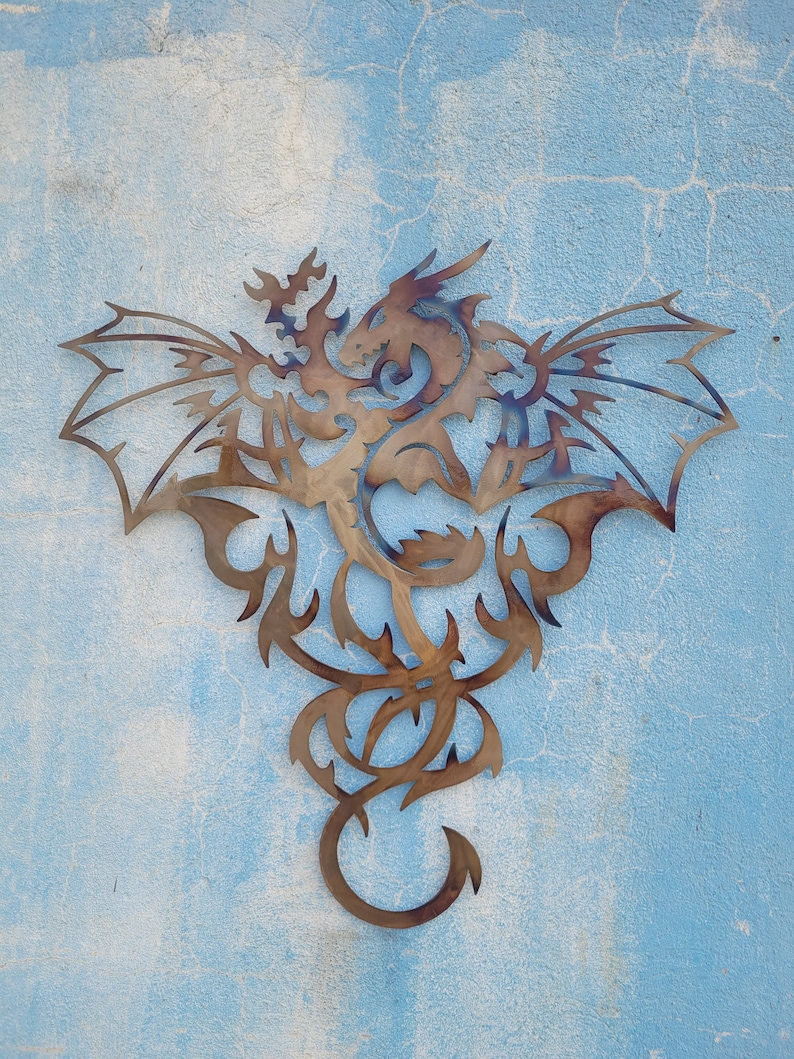 May include: A metal wall decor featuring a stylized dragon with intricate details. The dragon is depicted with wings spread wide and a long, flowing tail. The metal is a warm brown color, giving the piece a rustic look.