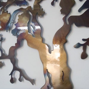 Op de afbeelding: Een metalen wandsculptuur van een boom met een bruine, gouden en blauwe iriserende afwerking. De takken van de boom zijn ingewikkeld en gedetailleerd, wat een uniek en modern ontwerp cre&euml;ert.