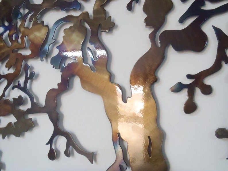 Op de afbeelding: Een metalen wandsculptuur van een boom met een bruine, gouden en blauwe iriserende afwerking. De takken van de boom zijn ingewikkeld en gedetailleerd, wat een uniek en modern ontwerp cre&euml;ert.