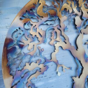 Op de afbeelding: Een metalen wandkunstwerk in de vorm van een boom met een blauwe, bruine en gouden iriserende afwerking.