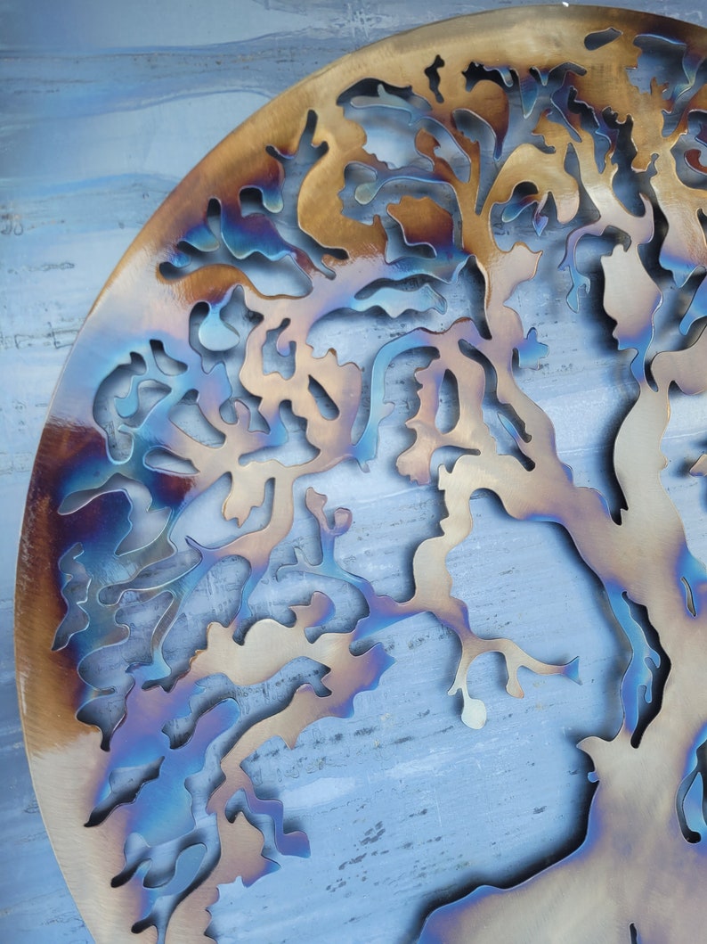 Op de afbeelding: Een metalen wandkunstwerk in de vorm van een boom met een blauwe, bruine en gouden iriserende afwerking.