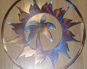 May include: A metal wall decor featuring a palm tree silhouette inside a circular sunburst design. The metal has a burnished finish with shades of blue, purple, and copper.