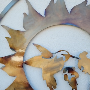 May include: A metal wall art sculpture featuring a hummingbird in flight, with a sunburst design behind it. The hummingbird is depicted in a golden colour, while the sunburst is a mix of gold and iridescent colours.