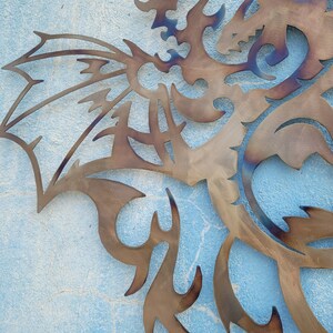 May include: A metal dragon sculpture with intricate details, cut out in a brown color, against a blue background.