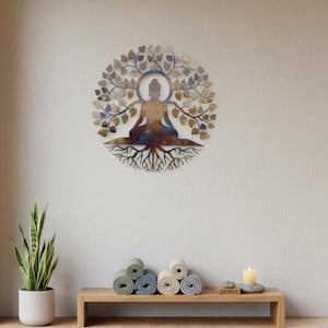 Könnte beinhalten: Ein kreisförmiges Wandkunstobjekt aus Metall, das die Silhouette einer sitzenden Person in Meditationshaltung zeigt, integriert in ein Baumdesign mit ausladenden Ästen, Blättern und Wurzeln in metallischen Bronze-, Blau- und Goldtönen.