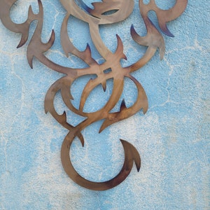 May include: A metal wall decor in the shape of a stylized dragon with intricate details. The dragon is a dark brown color and is set against a light blue background.