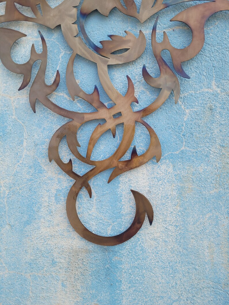 May include: A metal wall decor in the shape of a stylized dragon with intricate details. The dragon is a dark brown color and is set against a light blue background.