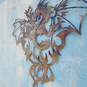 May include: A metal wall sculpture of a dragon with intricate details. The dragon is in a flying pose with its wings spread wide. The sculpture is made of a dark brown metal and has a rustic finish.