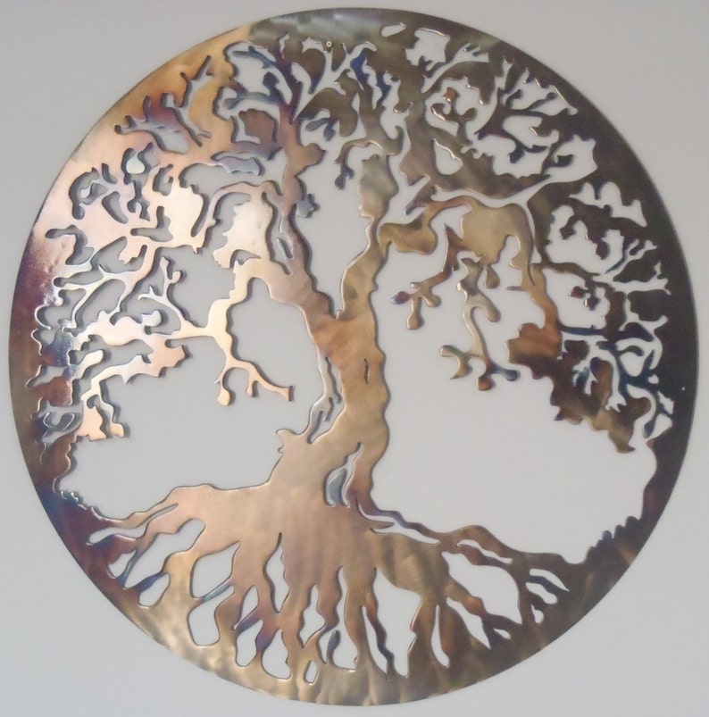 Op de afbeelding: Een cirkelvormige metalen wanddecoratie die een levensboom met ingewikkelde takken en wortels voorstelt. Het metaal heeft een geborstelde afwerking met een regenboogkleurige, iriserende glans.