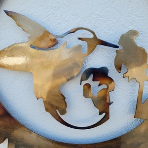 May include: A metal wall art piece depicting a hummingbird in flight with a palm tree in the background. The piece is cut out of metal and has a rustic, brown finish.