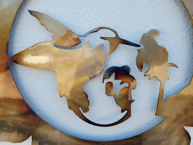 May include: A metal wall art piece depicting a hummingbird in flight with a palm tree in the background. The piece is cut out of metal and has a rustic, brown finish.
