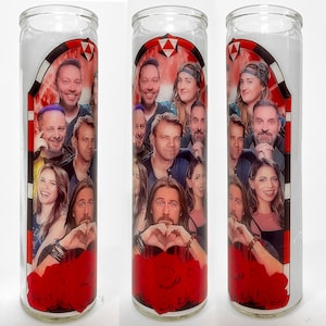 May include: A glass candle with a red, white and black design featuring a group of people. The candle has a red rose design at the bottom.
