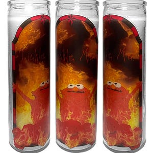 Könnte beinhalten: Drei Gebetskerzen aus Glas mit einem rot-schwarzen Etikett mit einer Cartoonfigur in Flammen. Der Text "Tickle Me" ist auf dem Etikett zu sehen. Die Kerzen sind mit weißem Wachs gefüllt.