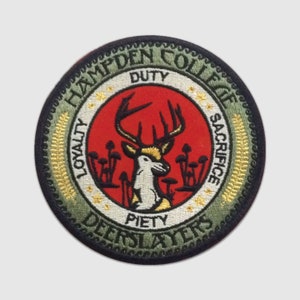 May include: A green and gold embroidered patch with a black outline. The patch features a white deer with antlers standing in a red circle. The words "Hampden College" are written in a black circular banner around the deer. The words "Loyalty, Duty, Piety, Sacrifice" are written in a black circular banner around the deer. The words "Deerslayers" are written in a black circular banner around the deer.