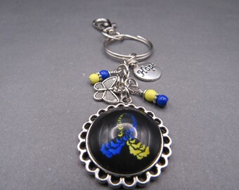 May include: A silver keychain with a black and white butterfly charm, blue and yellow beads, and a silver charm that says "Hope". The keychain also features a round, silver-framed charm with a black background and a yellow and blue ribbon design.