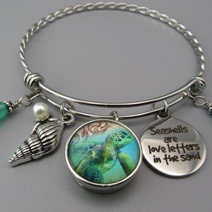 May include: Silver charm bracelet with a sea turtle, seashell, and a charm that says "Seashells are love letters in the sand". The bracelet also has two green glass beads.