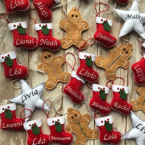 May include: A collection of felt Christmas ornaments featuring gingerbread people, stockings, and stars. Each ornament is personalized with a name, including names like "Lionel", "Noah", "Léo", "Livio", "Summer", and "Mathys".
