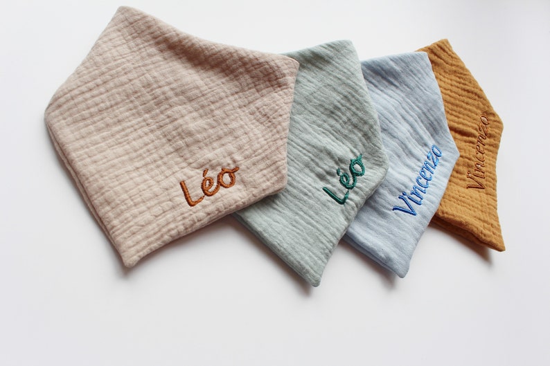 May include: Four personalized baby bibs in different colors and fabrics. The bibs are embroidered with the names "L&eacute;o", "L&eacute;o", and "Vincenzo".