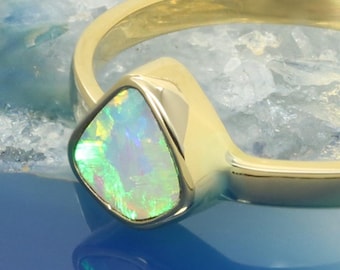 May include: A gold ring with a triangular opal gemstone. The opal is a light green color with flashes of blue and white.