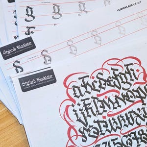 May include: A collection of calligraphy workbooks and a black marker. The workbooks feature stylized blackletter alphabets and numbers, with examples and guides. The text "Stylized Blackletter" is visible on the covers.