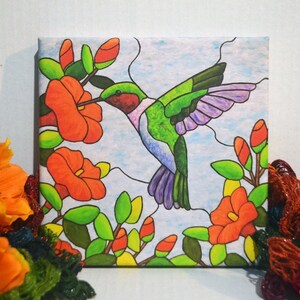 May include: A canvas print of a hummingbird in flight, with green, purple, and black wings, drinking nectar from a red flower. The background is a light blue with white clouds.