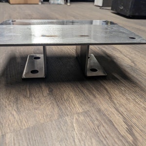 May include: A silver metal plate with two metal supports underneath. The plate is rectangular and has rounded corners. The supports are shaped like an H and have holes in them.