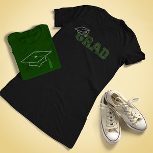 Könnte beinhalten: Schwarzes T-Shirt mit grünen Strasssteinen, die "GRAD" und eine Abschluss-Kappe buchstabieren. Ein grünes T-Shirt mit einer grünen Strass-Abschluss-Kappe liegt auf dem schwarzen T-Shirt.