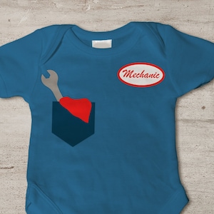 May include: A blue baby onesie with a red heart and a wrench in a pocket. The onesie has a red oval patch with the word "Mechanic" on it.