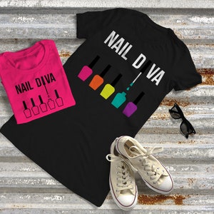 May include: Two black t-shirts with the text "Nail Diva" and a graphic of nail polish bottles. The t-shirts are folded and laid out on a metal surface.