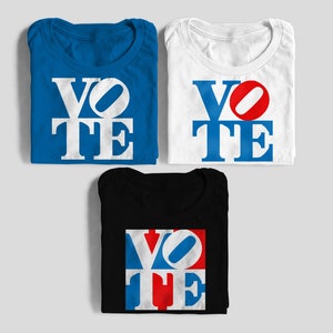 May include: Three folded t-shirts in blue, white, and black. Each shirt displays the word "VOTE" in a bold, stylized font. The blue shirt has white letters, the white shirt has blue letters with a red accent, and the black shirt has a red, white, and blue design.
