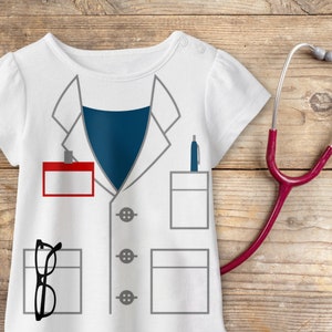 May include: White t-shirt with a printed design of a doctor's coat, including a name tag, pockets, and buttons. A stethoscope, glasses, and a pen are also included in the design.