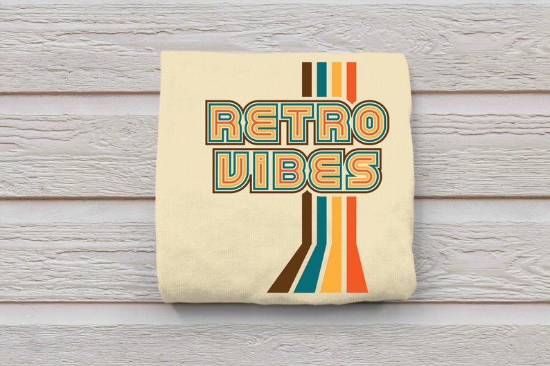 May include: A beige t-shirt with the text "Retro Vibes" in a retro font with colorful stripes. The text is in a multi-colored font with brown, teal, yellow, and orange stripes.