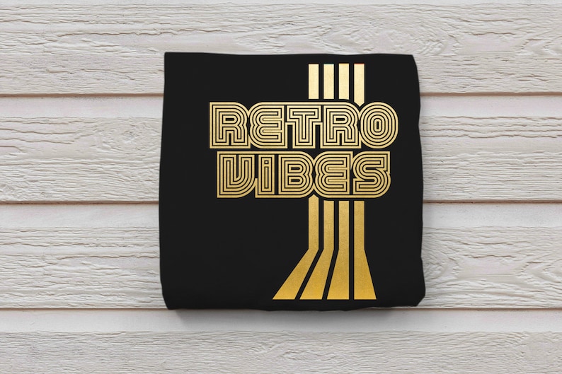 May include: Black t-shirt with gold foil lettering that reads "Retro Vibes" in a retro font style. The lettering is outlined with a thin black line. There are five vertical gold lines to the right of the text.