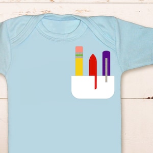 May include: A light blue baby onesie with a white pocket. The pocket has a red, yellow, and purple pencil and pen inside.