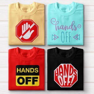 May include: Four t-shirts with different designs. The first is beige with a red stop sign with a hand and the text "Hands Off". The second is light blue with the text "Hands Off" in purple. The third is red with a yellow rectangle with the text "Hands Off". The fourth is black with a red stop sign with the text "Hands Off!" in white.